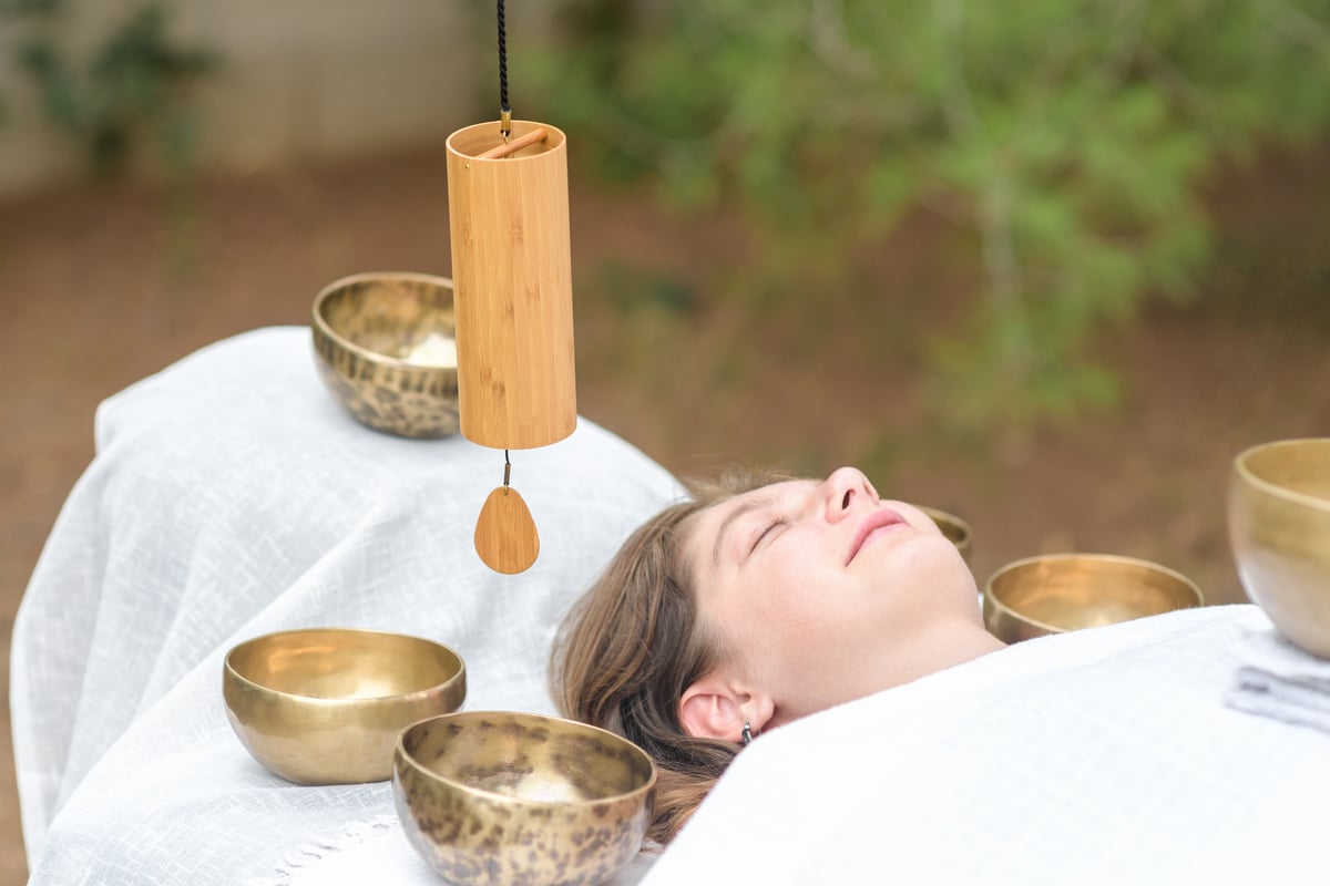 Male hand holding a bamboo Koshi chime during sound healing therapy with tibetan singing bowls over young woman outdoor